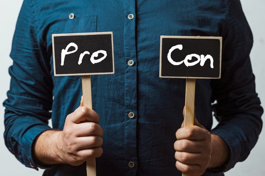 Photograph of a man holding two small signs in each hand. One sign says "Pro" the other sign says "Con".