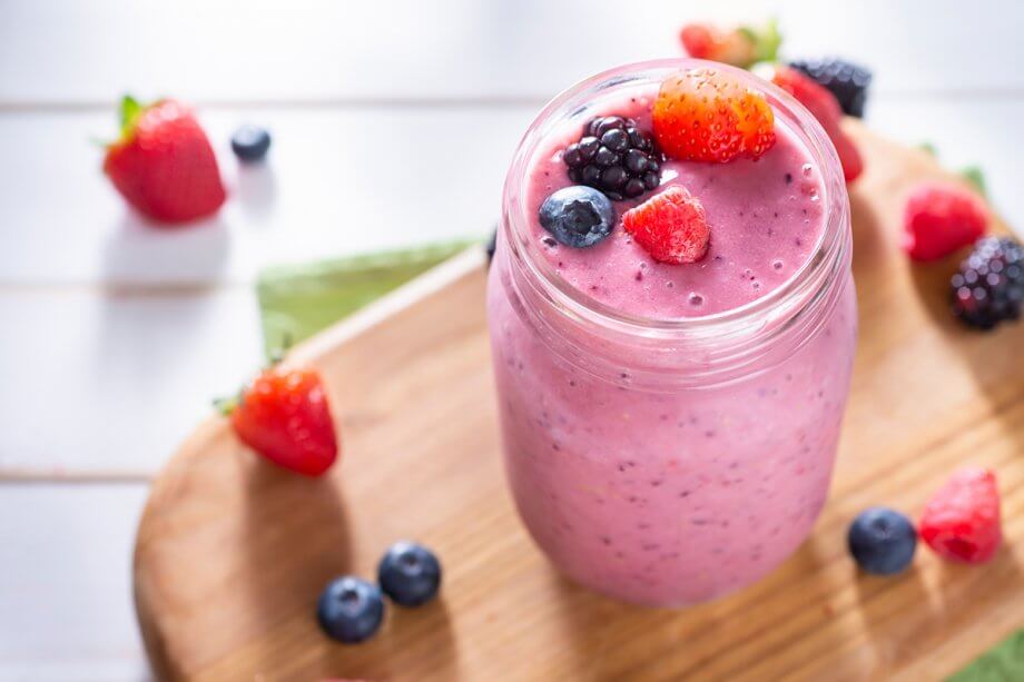 pink berry smoothie in mason jar sitting on wooden board with loose berries around it