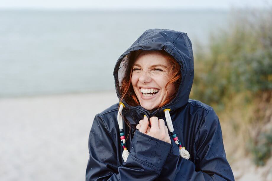 smiling woman standing outside in the rain with a navy raincoat on