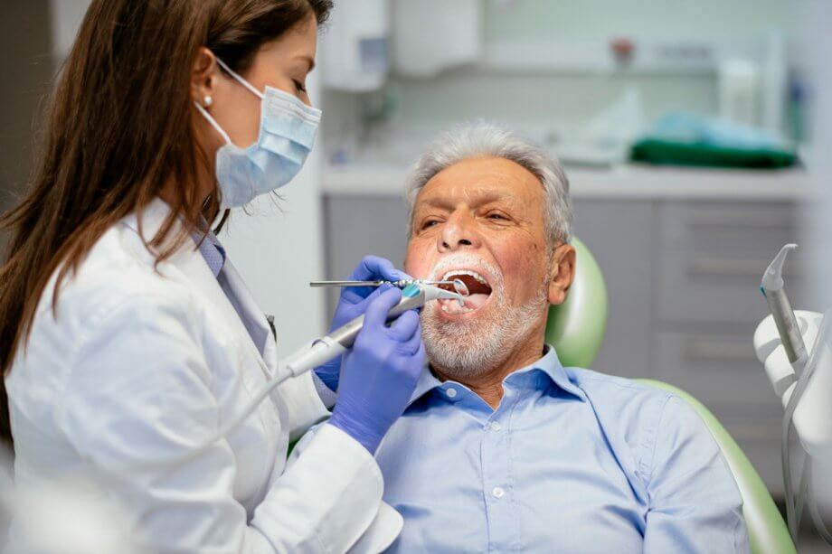 dentist examining an older male patient seated in an exam chair