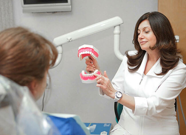 Dr. Alekseyeva showing a patient a plastic model of teeth, pointing to it