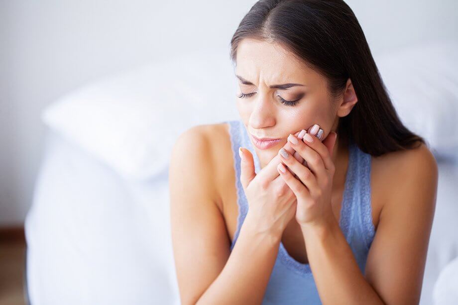 young woman sitting on bed holding her jaw in pain