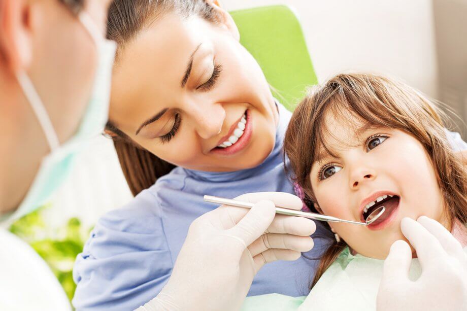 young girl sitting in mother's lap getting a dental exam from dentist