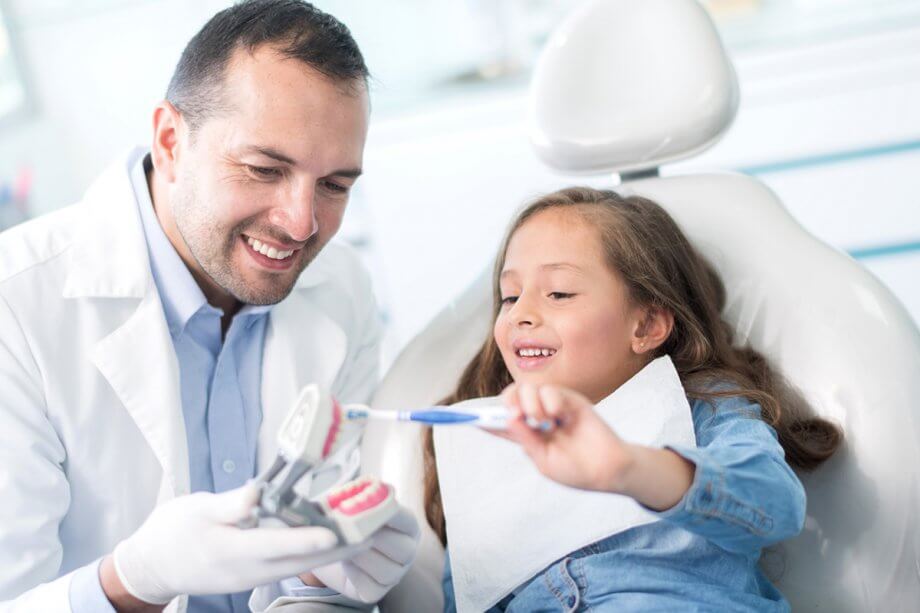 dentist holding model of teeth showing a young female patient how to brush her teeth